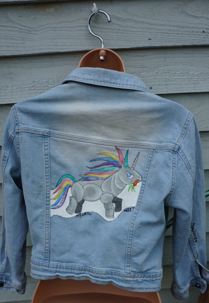 denim jacket with a cartoon image of a robot unicorn on it with a pastel rainbow tail and mane