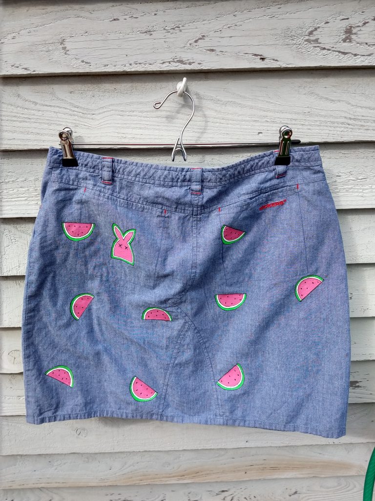 picture of the back of the skirt. it is a denim skit with randomly placed melon slices that are painted onto it. There is a pocket on the left butt side with a picture of a bunny shape in the same greenand pink colur as the melons.