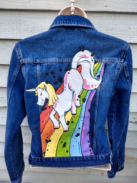 the back of a dnim jacket with an unicorn drawn in cartoon style riding down a rainbow