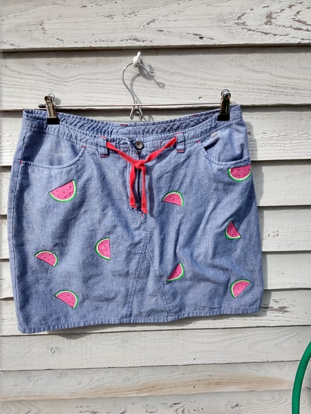 picture of a denim skirt with a red tie at the waist. It has small melon slices painted onto it in a random placement.
